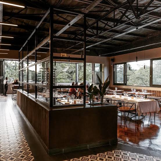 Warm restaurant interior with steel-framed bar, garden views and set tables